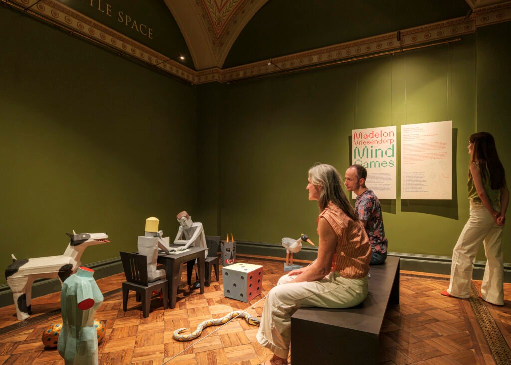 Three people in a green-walled room look at the new Madelon Vriesendorp exhibition.