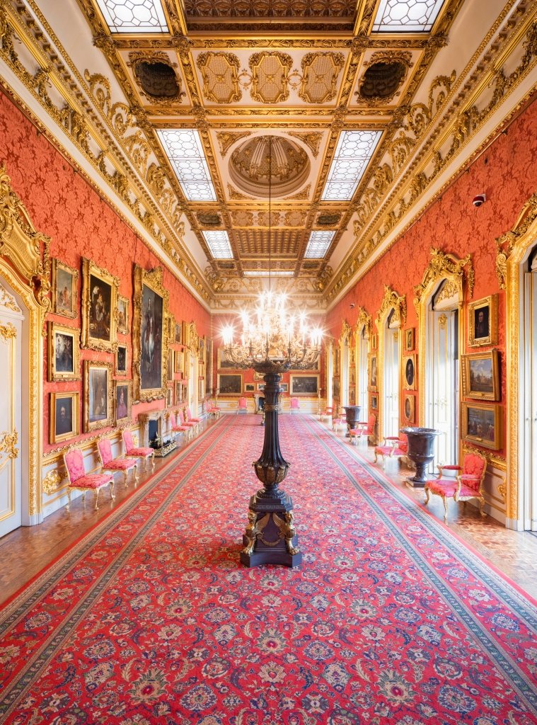 The Waterloo Gallery in Apsley House, a grand room with chandeliers, red wall hangings, gold decorations, and many historic portraits.