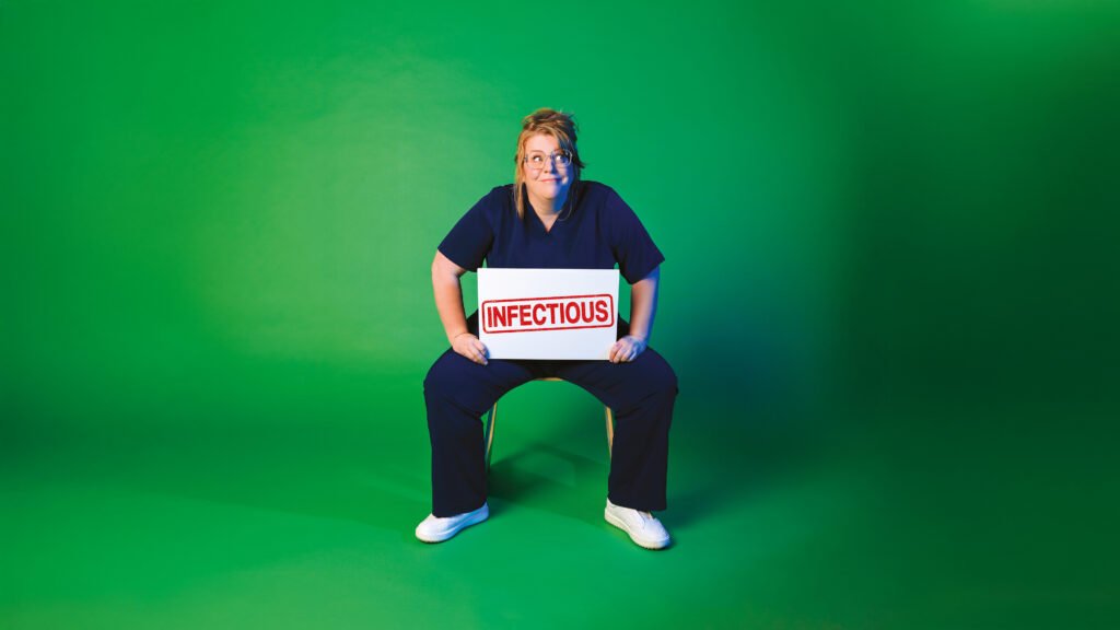 Georgie Carroll sat on a chair holding a sign that reads INFECTIOUS