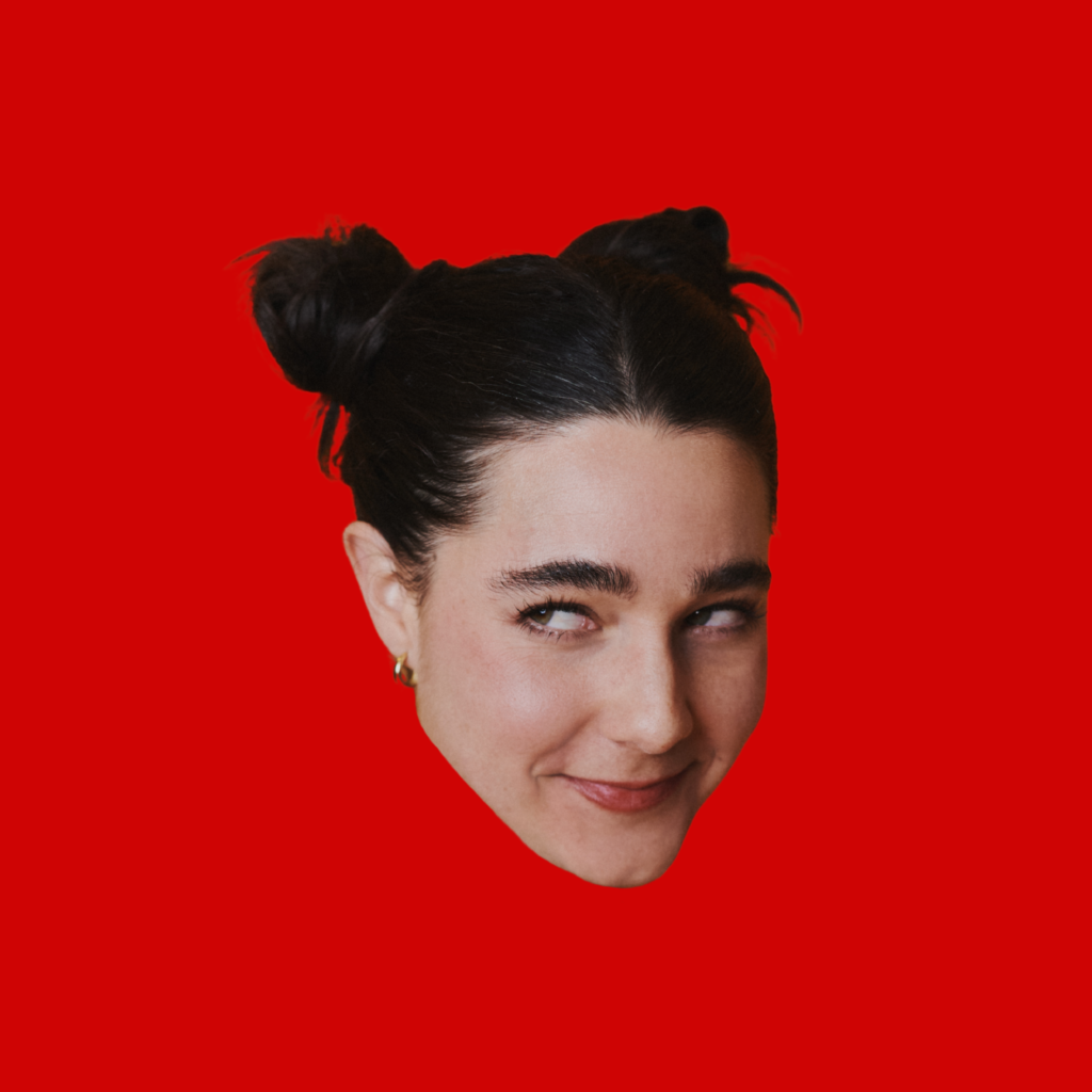 Lara Ricote smiles mischievously and looks to the side, her dark hair styled in two buns, against a bold red background.